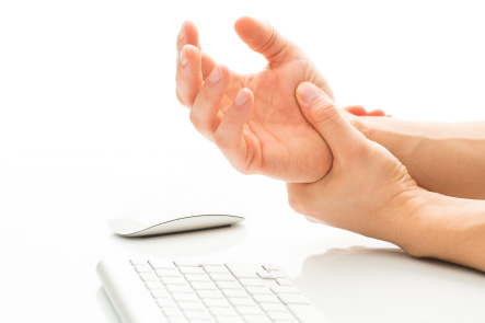 A close-up of someone holding their sore wrist beside a keyboard